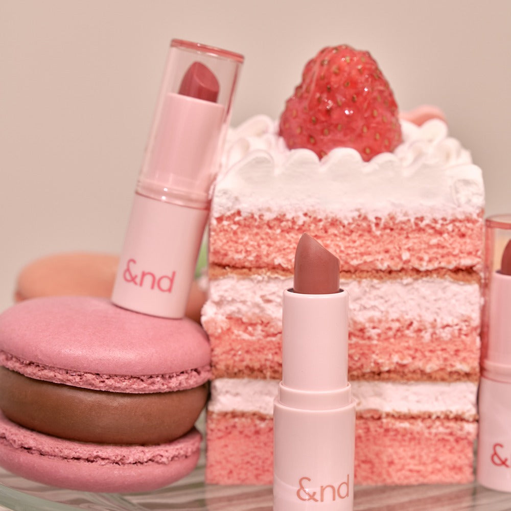 ROMAND Glassy Bomb Balm en packaging, posé près de desserts fraise et macarons, contexte beauté studio