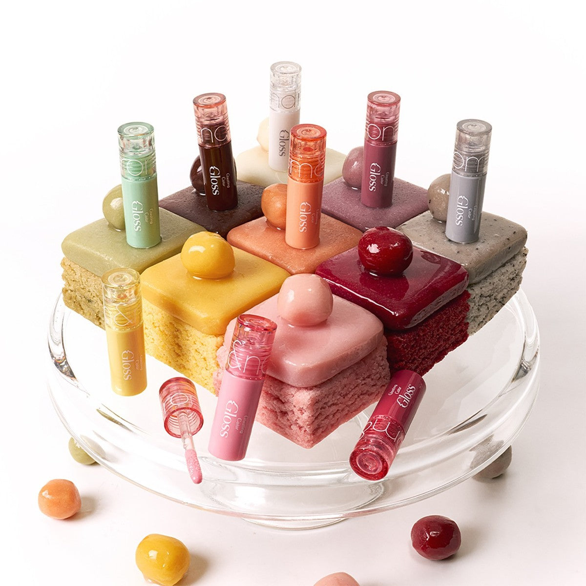 ROMAND MINI Glasting Color Gloss de la marque ROMAND, sur un plateau visuel avec mini gâteaux colorés.