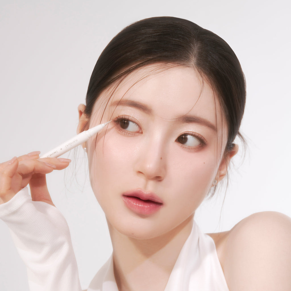 ROMAND Twinkle Pen Liner, stylo traceur yeux sur le visage, main en action maquillage lumineux sur fond clair.