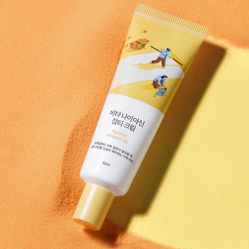 ROUND LAB Vita Niacin Spot Cream 50ml, tube crème sur fond orange texturé, marque ROUND LAB en contexte maquillage