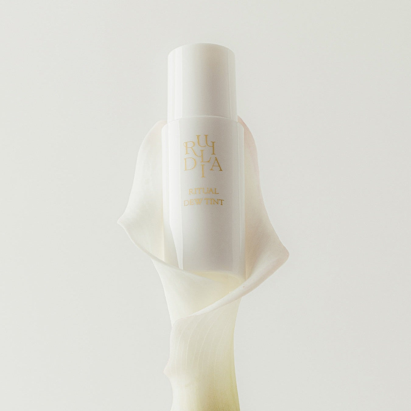 RULIDIA Ritual Dew Tint de la marque RULIDIA, flacon illuminé sur fond crème, mise en scène minimaliste.
