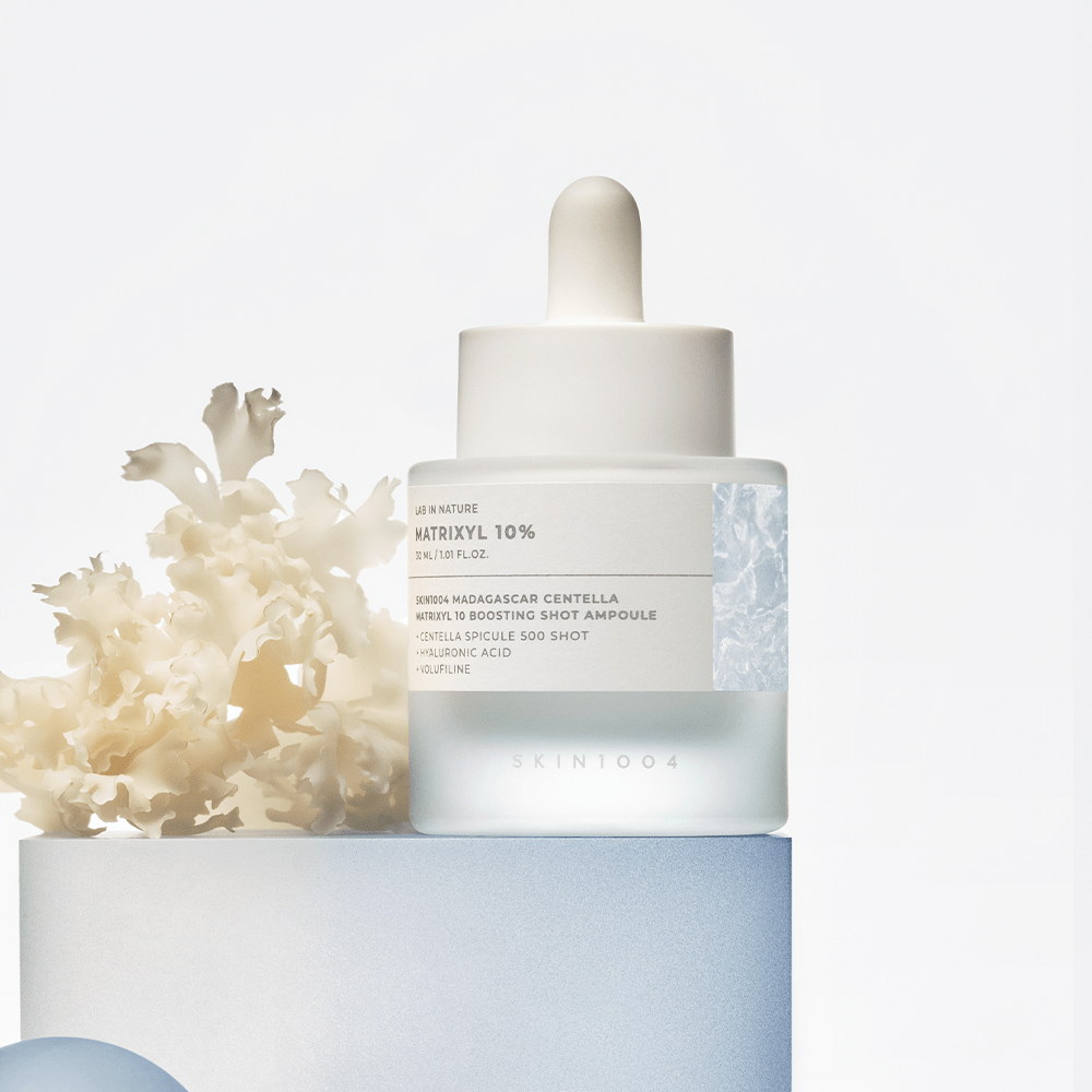 SKIN1004 Madagascar Centella Matrixyl 10 Boosting Shot Ampoule 30ml, flacon blanc sur fond clair avec fleurs en arrière-plan.