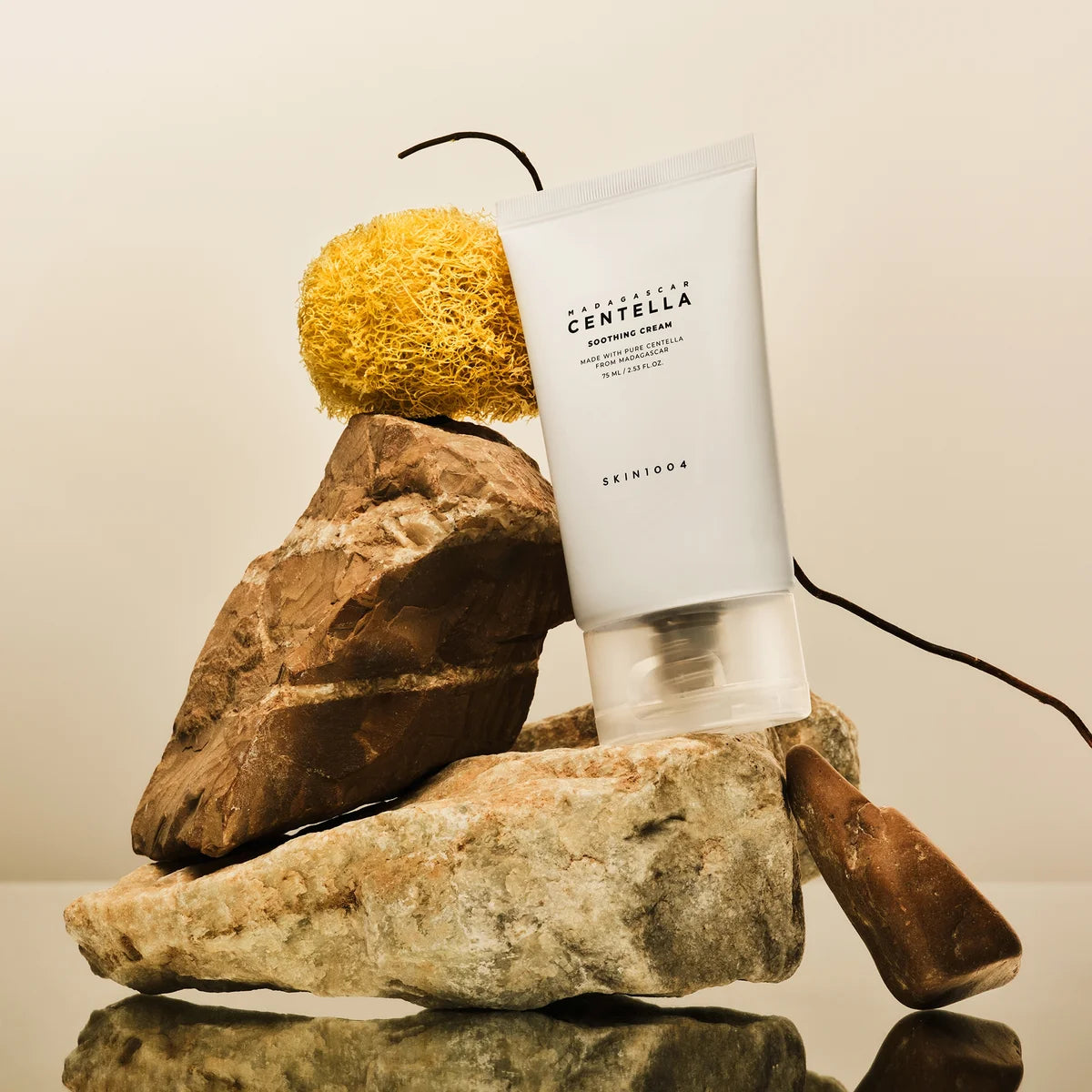 SKIN1004 Madagascar Centella Soothing Cream 75ml, tube SKIN1004 sur galets et éponge, contexte beauté spa.