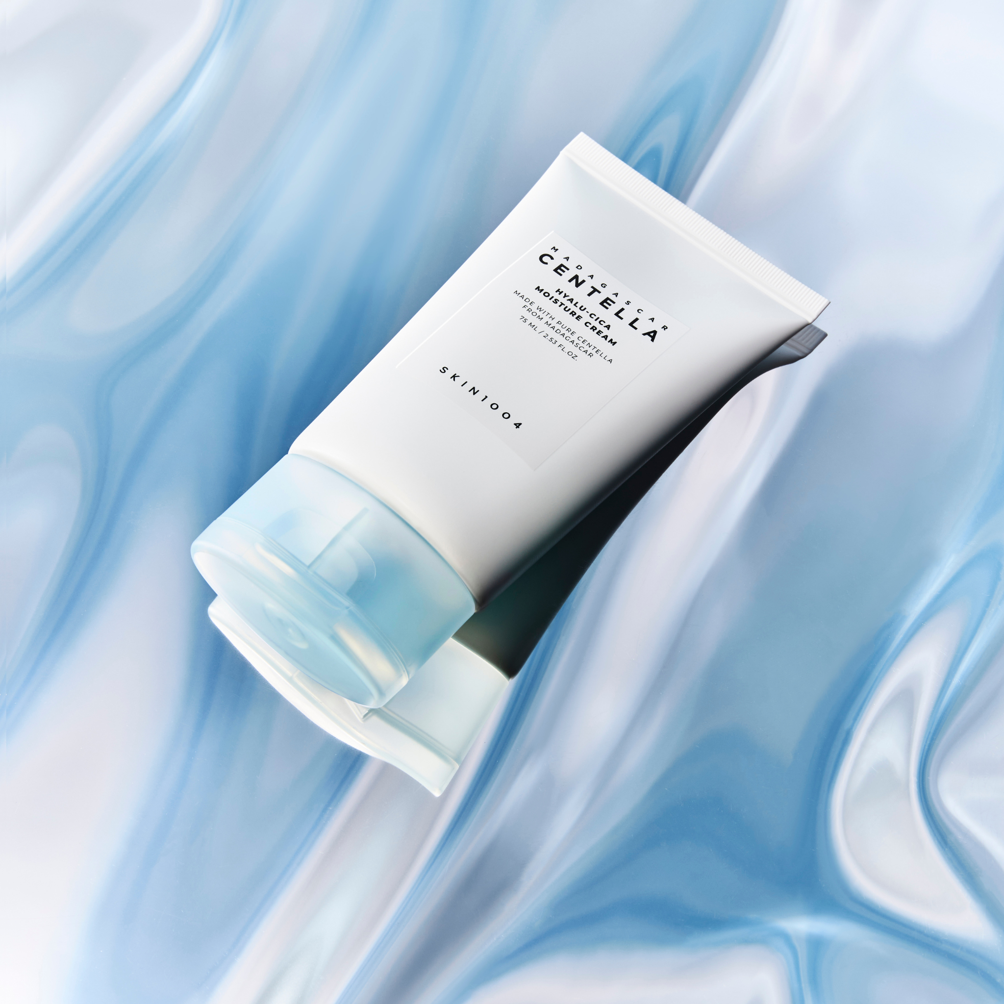 Crème hydratante SKIN1004 Madagascar Centella Hyalu-Cica Moisture Cream 75ml posée sur un fond bleu aquatique.