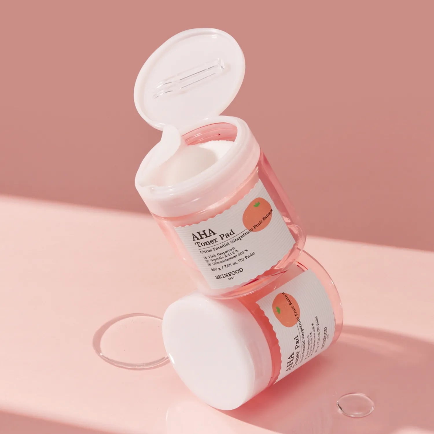 SKINFOOD Pink Grapefruit AHA Toner Pad 70 sheets, pads et flacon ouverts sur fond rose, packshot produit marque SKINFOOD