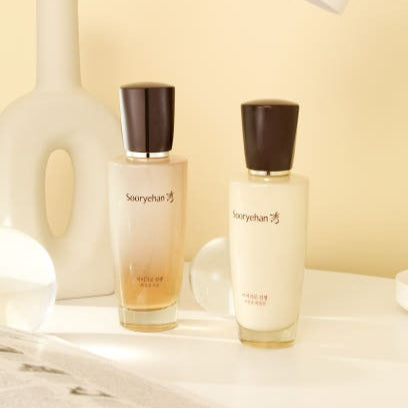 Deux bouteilles de SOORYEHAN Micro Ginseng Essentail Emulsion 130ml sur une table blanche avec fond beige.