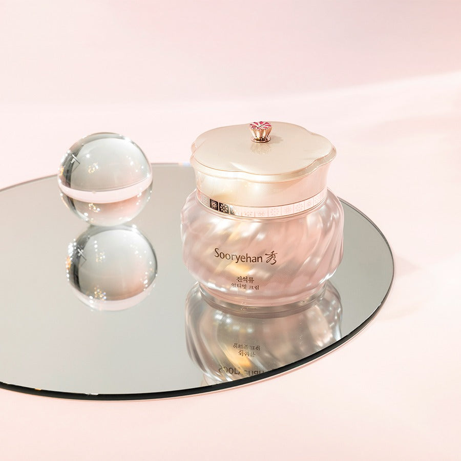 Crème "SOORYEHAN Ultimate Cream 50ml" posée sur un miroir, emballage élégant et perle brillante à côté, cosmétique haut de gamme.
