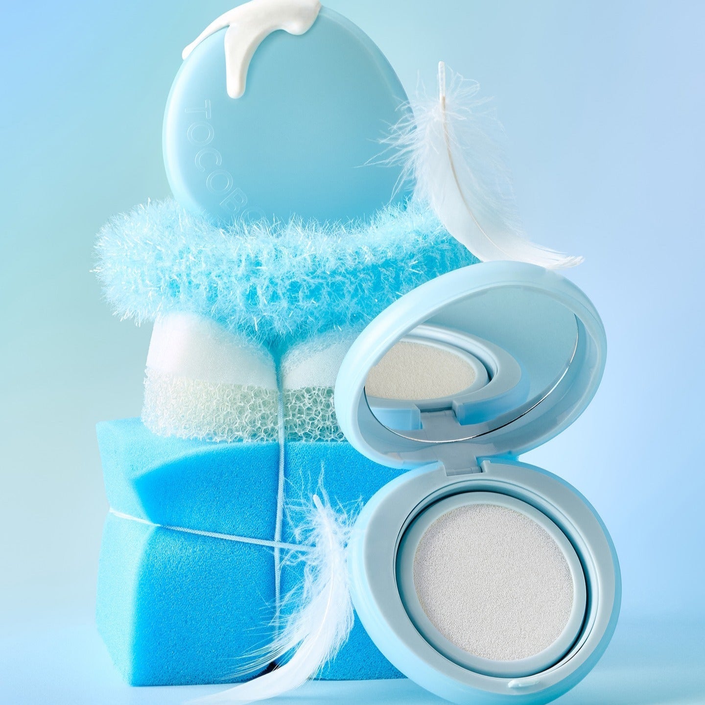 TOCOBO Blur Finish Sun Cushion, boîtier maquillage bleu sur fond ciel, texture poudre floue, style beauté.