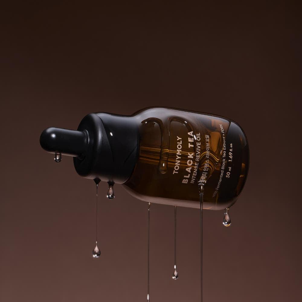 TONY MOLY Black Tea Intense Revive Oil 50ml, flacon noir versé sur fond brun, gouttes et texture huileuse