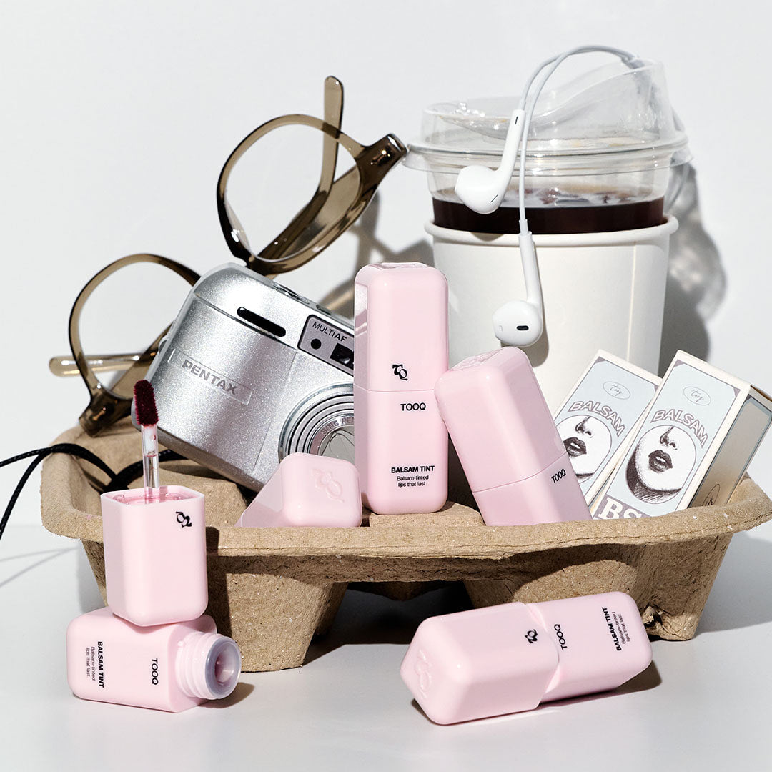 TOOQ Balsam Tint de la marque TOOQ, produits cosmétiques roses sur fond clair, lunettes et accessoires en contexte visuel