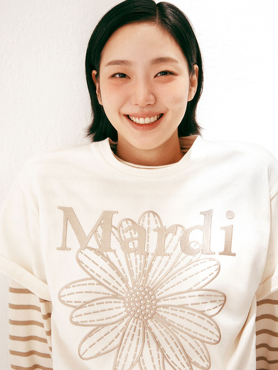 TSHIRT FLOWERMARDI NEEDLEWORK_CREAM BEIGE Mardi Mercredi : mannequin souriant, t-shirt crème avec broderie fleur, fond clair.