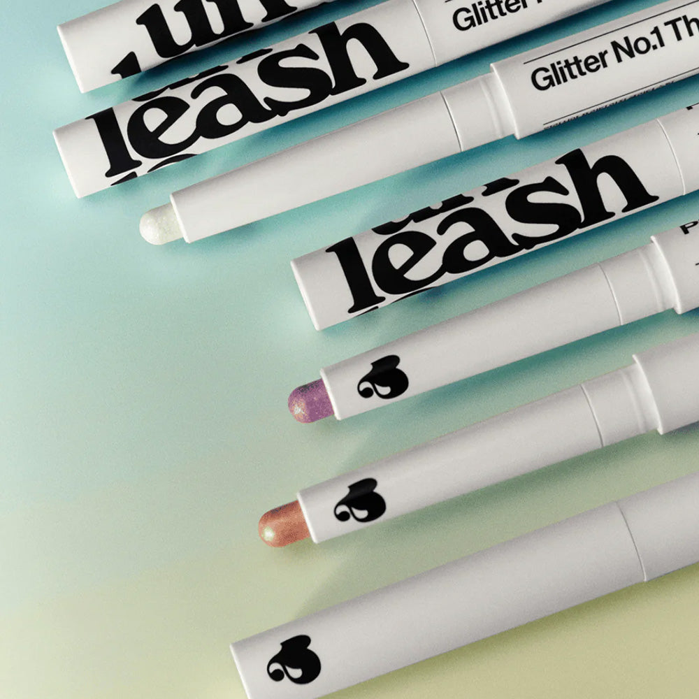 Lignes de UNLEASHIA Pretty Easy Glitter Stick sur fond pastel, parfait pour des maquillages scintillants et glamour.