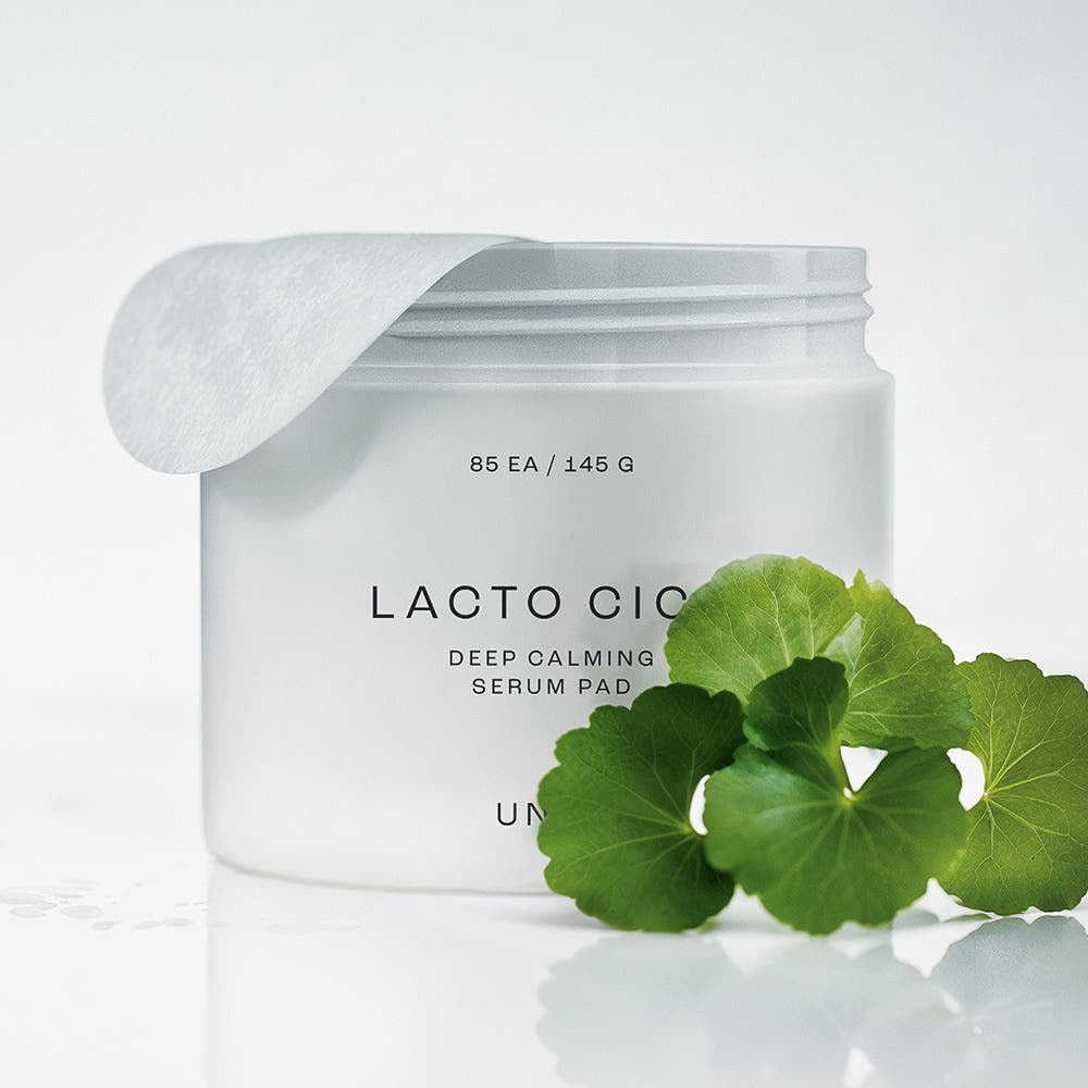 Décris l'image en français : UNPA Lacto Cica Deep Calming Serum Pad 85 Sheets, sérum pads UNPA sur fond blanc avec feuilles de cica.