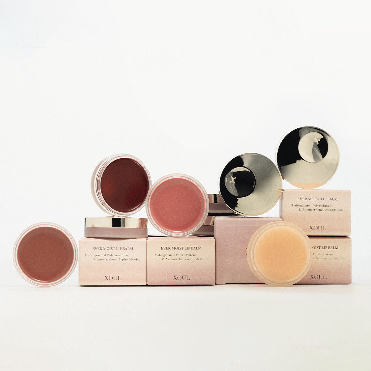 Décris l'image en français : XOUL Ever Moist Volume Lip Balm 8g de la marque XOUL, baumes sur fond blanc, étuis et couvercles dorés.