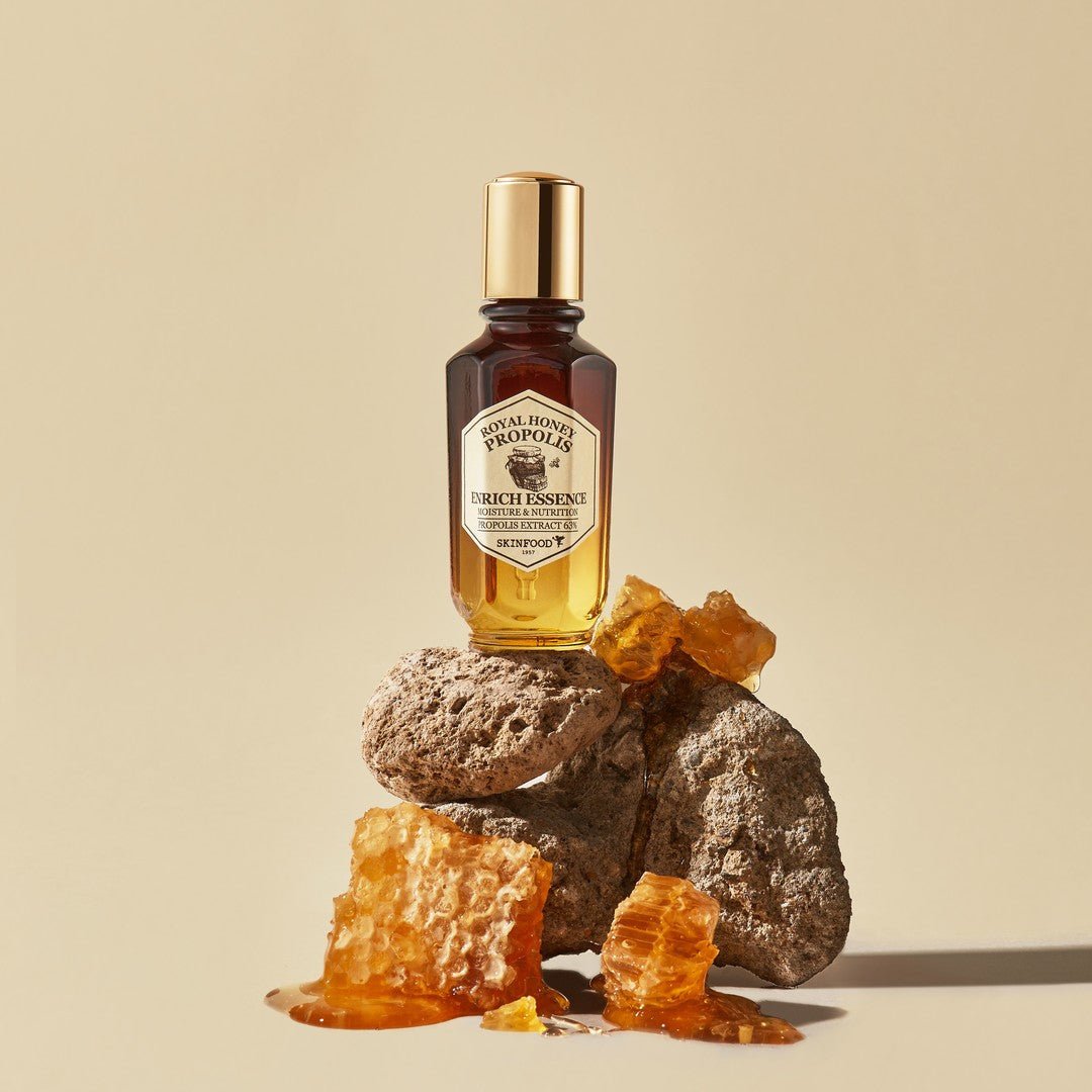SKINFOOD Royal Honey Propolis Enrich Essence 50ml, bouteille SKINFOOD sur fond beige avec miel et pierre dorée, photo produit