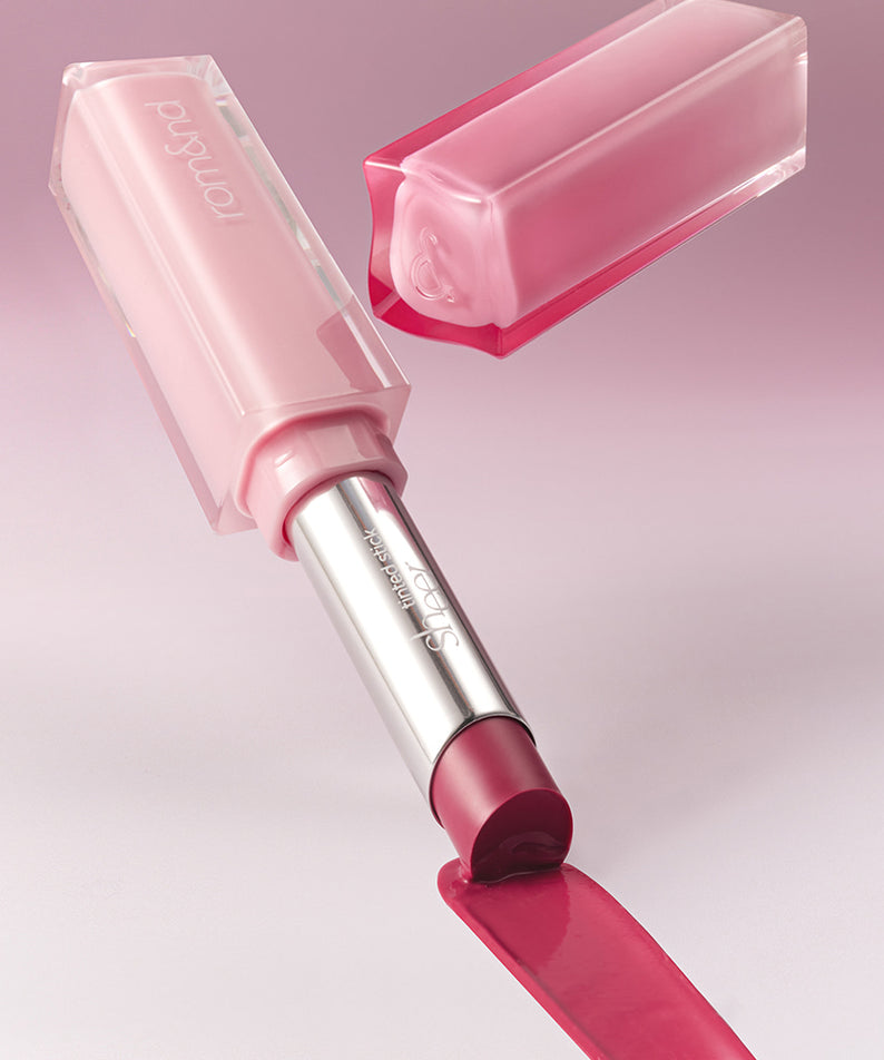 ROMAND Sheer Tinted Stick de la marque ROMAND, stick rose translucide sur fond rose, maquillage en gros plan.