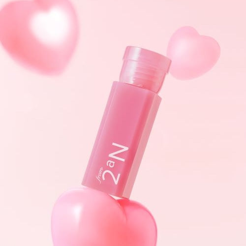 Décris l'image en français : 2AN Mini Glaze Bouncing Tint de 2AN, flacon rose sur fond pastel avec cœurs flous.