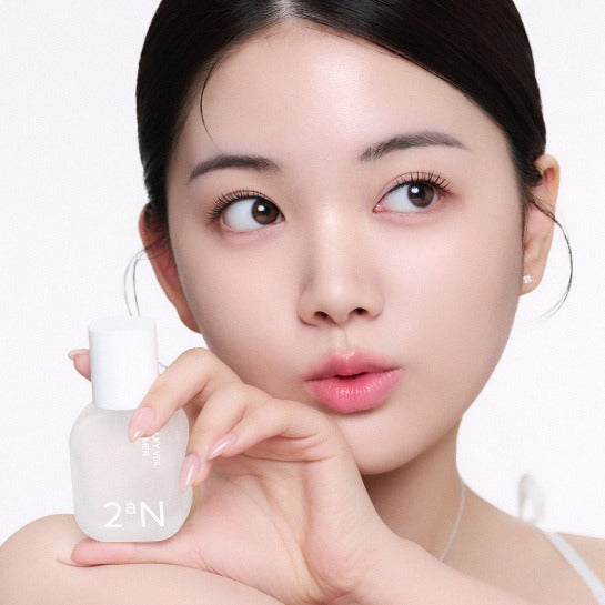 Décris l'image : 2AN Silky Veil Primer de 2aN, visage maquillé et pot de primer sur fond clair, femme en gros plan