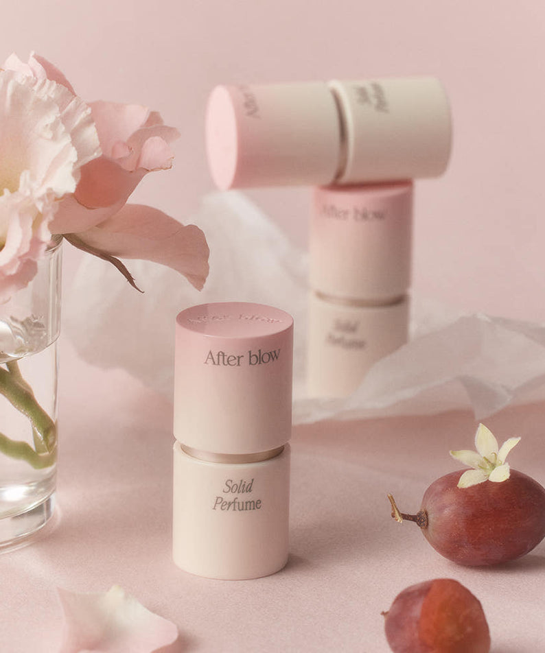 AFTER BLOW Solid Perfume 6.5g, baume parfumé en stick sur fond pastel, fleurs et accessoires décoratifs.