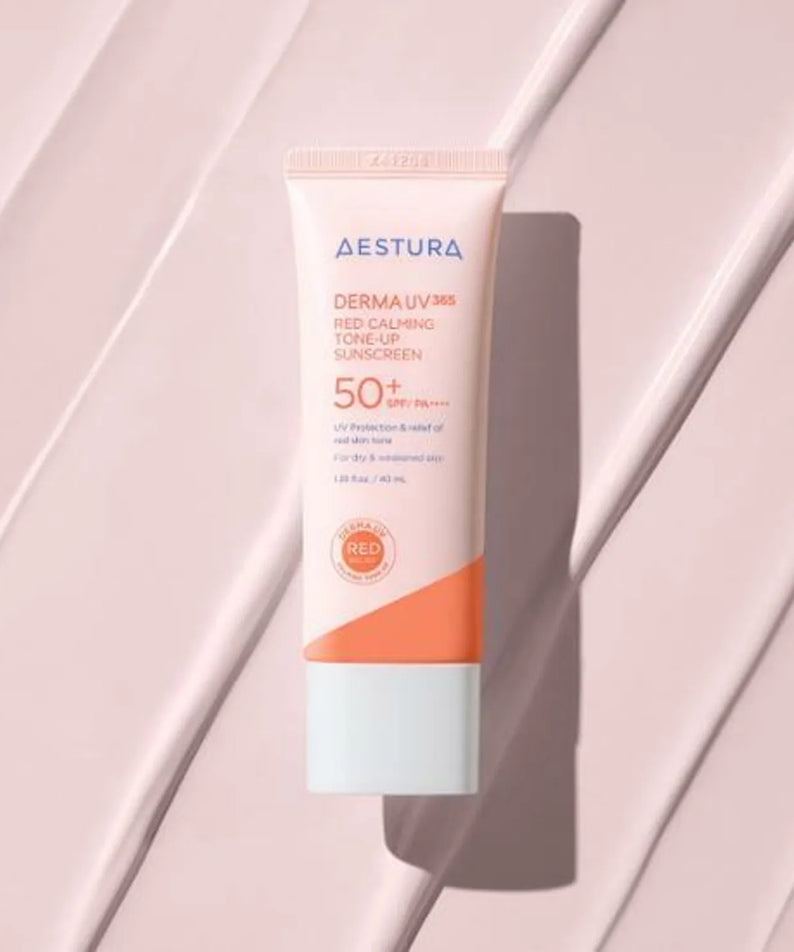 Décris l'image en français : AESTURA Derma UV365 Red Calming Tone-Up Sunscreen 40ml, tube AESTURA sur tissu rose