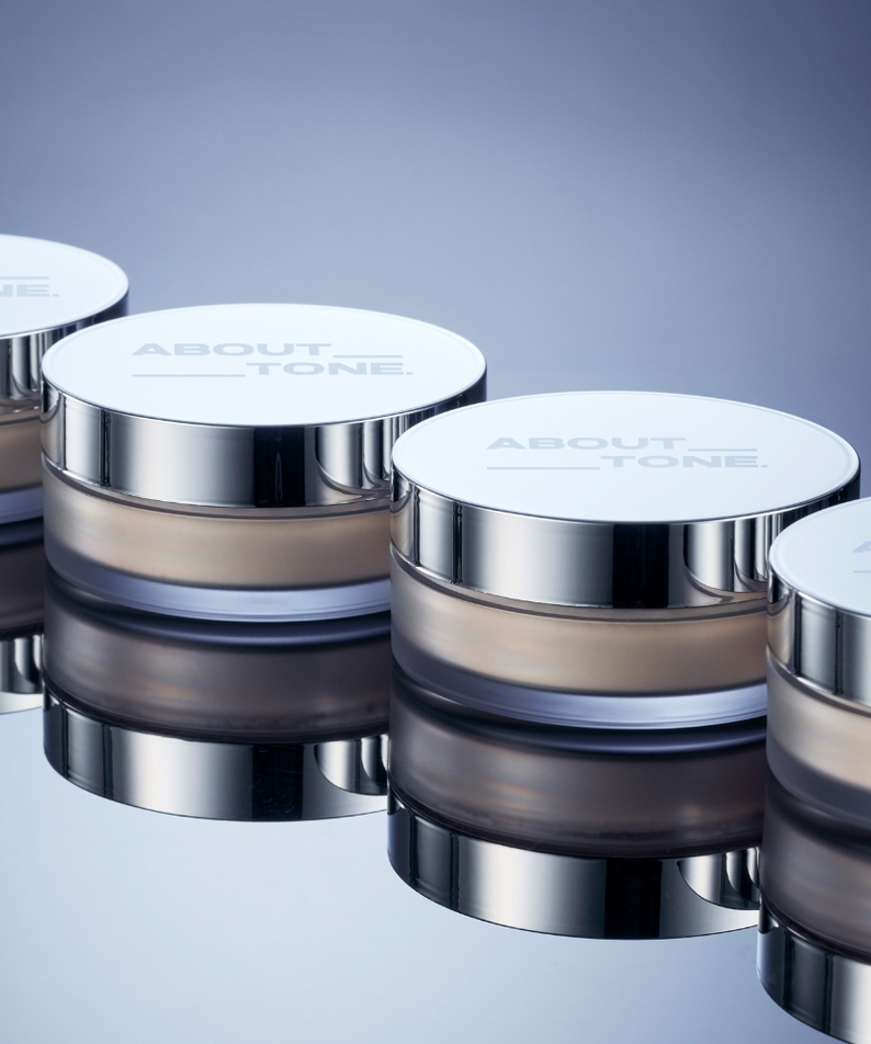 ABOUT TONE The Blur Finish Powder, pots argentés sur fond bleu, mise en scène maquillage produit de la marque ABOUT TONE.