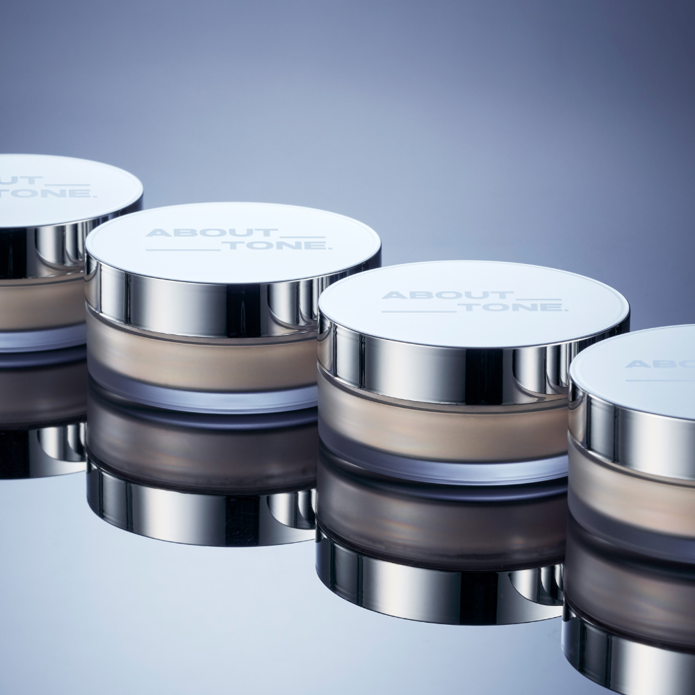 ABOUT TONE The Blur Finish Powder, pots argentés sur fond bleu, mise en scène maquillage produit de la marque ABOUT TONE.