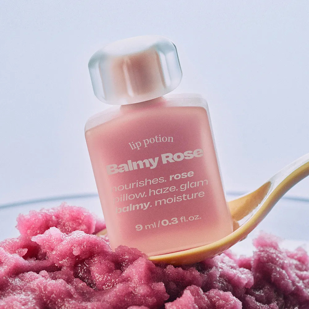 ALTERNATIVE STEREO Lip Potion Balmy Rose, baume lèvres rosé sur fond clair avec texture rose et cordon doré, studio.
