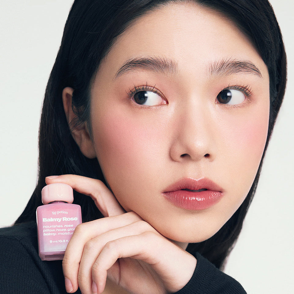 ALTERNATIVE STEREO Lip Potion Balmy Rose, baume rosé sur fond clair, femme tient le produit maquillage lèvres
