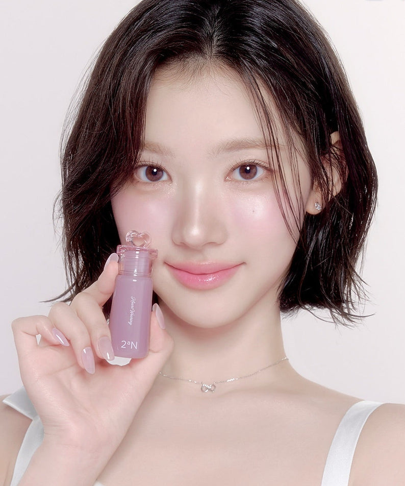 Femme souriante tenant le 2AN Heart Wearing Liquid Cheek 4.4g, maquillage tendance pour les joues, teinte liquide rose en flacon.