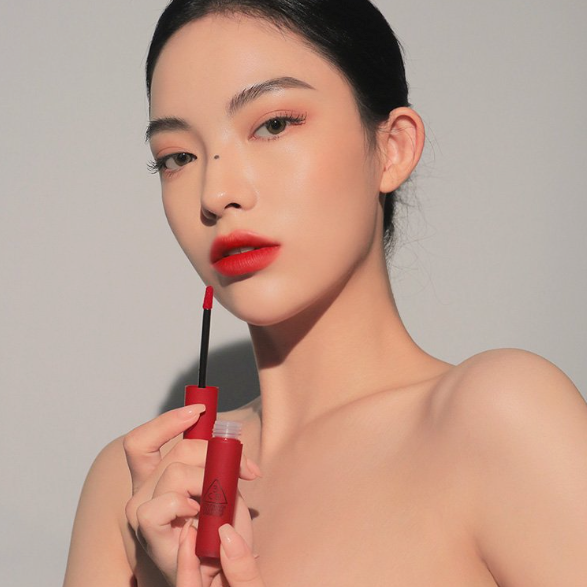 3CE Blurring Liquid Lip 10 shades : femme maquillée tenant le rouge à lèvres 3CE, fond clair, photo produit