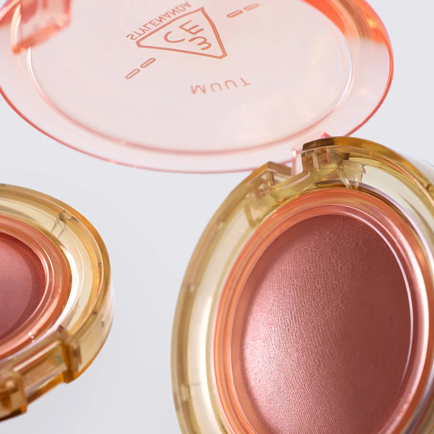 Gros plan sur 3CE Bouncy Blur Balm de 3CE, baume teinté dans son étui doré, texture rosée sur fond clair