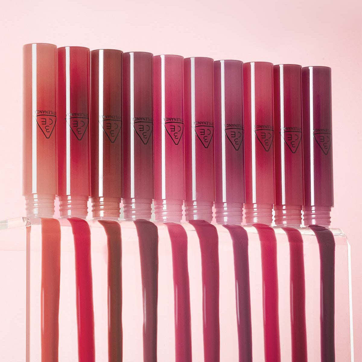 3CE Drop Glow Gel 10 Shades, tubes brillants en dégradé rouge sur fond rose, pack produit de la marque 3CE.