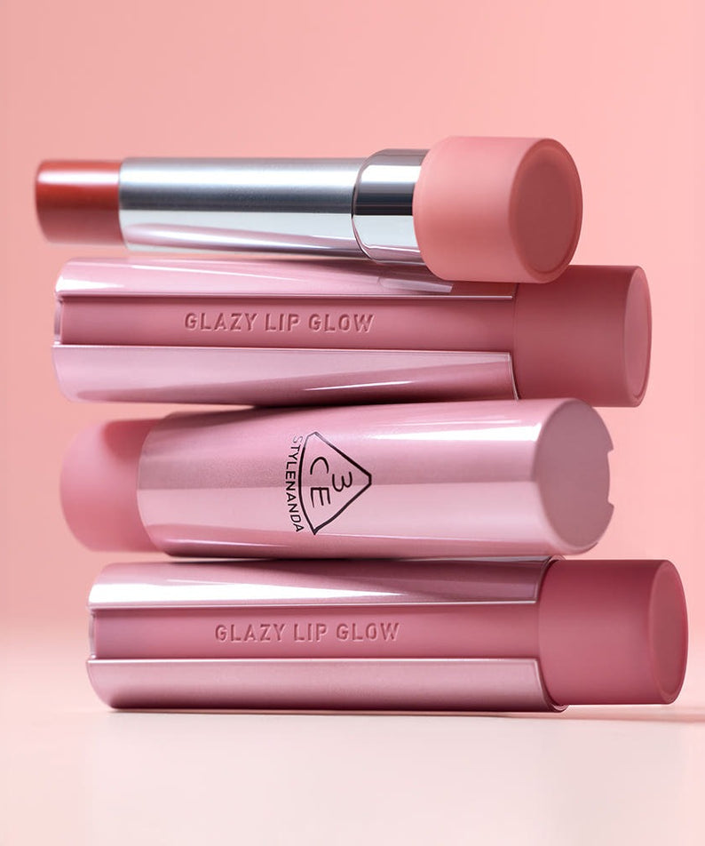3CE Glaze Lip Glow 3.2g, produit de la marque 3CE : gloss pour lèvres, sur fond rose, tubes empilés, maquillage
