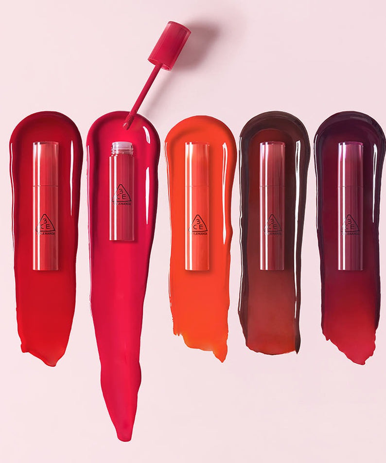 3CE Lazy Pop Lip Stain de 3CE, tubes de gloss aux teintes rouges et brunes sur fond rose pastel.