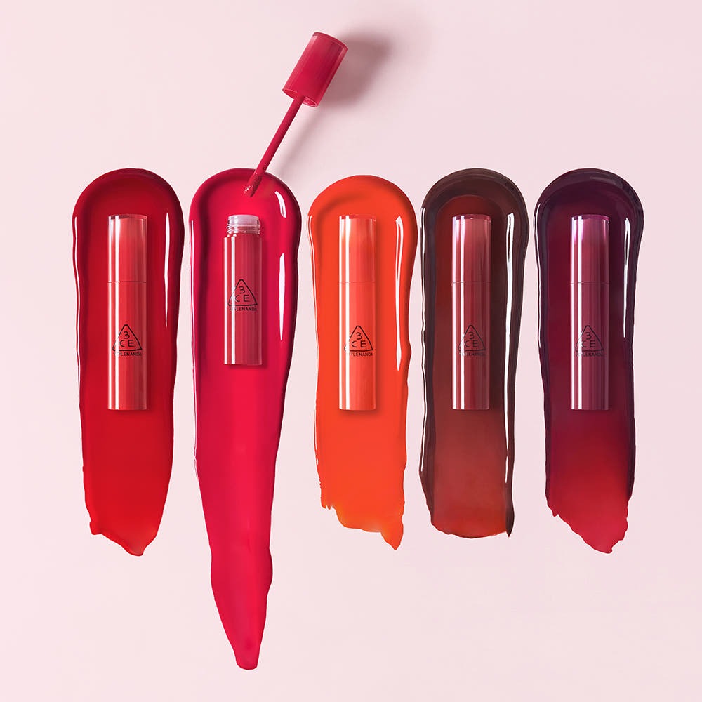 3CE Lazy Pop Lip Stain de 3CE, tubes de gloss aux teintes rouges et brunes sur fond rose pastel.