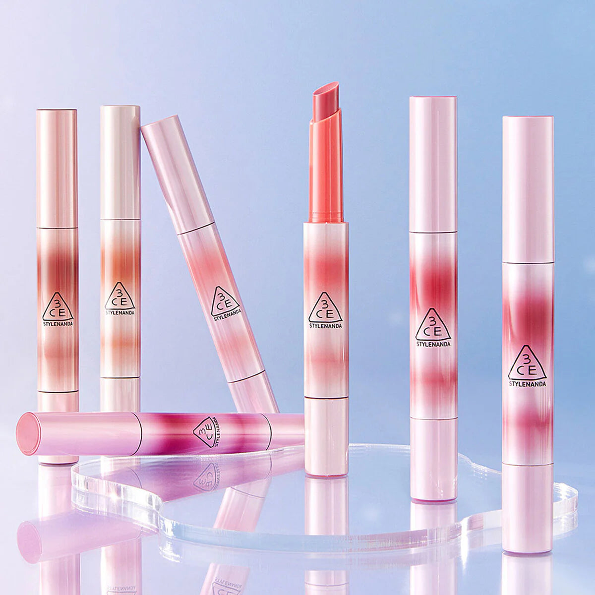 3CE Shine Reflector 8 shades de 3CE, sticks brillants sur fond bleu, maquillage reflets lumineux et élégant.