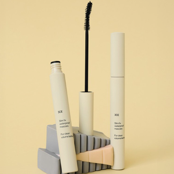 3CE Slim Fix Waterproof Mascara, maquillage yeux, flacon et brosse sur fond beige, marque 3CE en mise en scène.