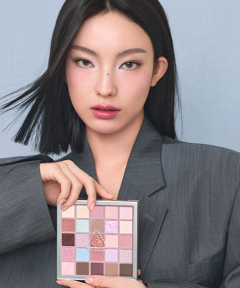 3CE XL Eyeshadow Palette : femme maquillée tenant la palette, sur fond bleu clair, lumière douce, vue rapprochée.