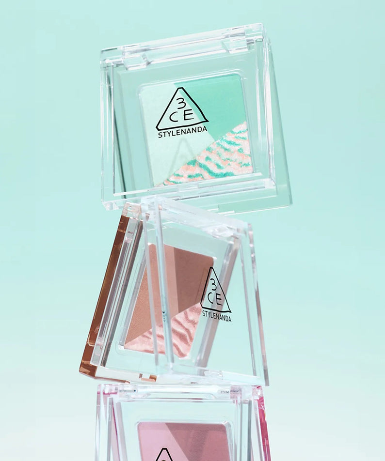 Empilement de fards à paupières 3CE Color Grid Eyeshadow sur fond turquoise lumineux.