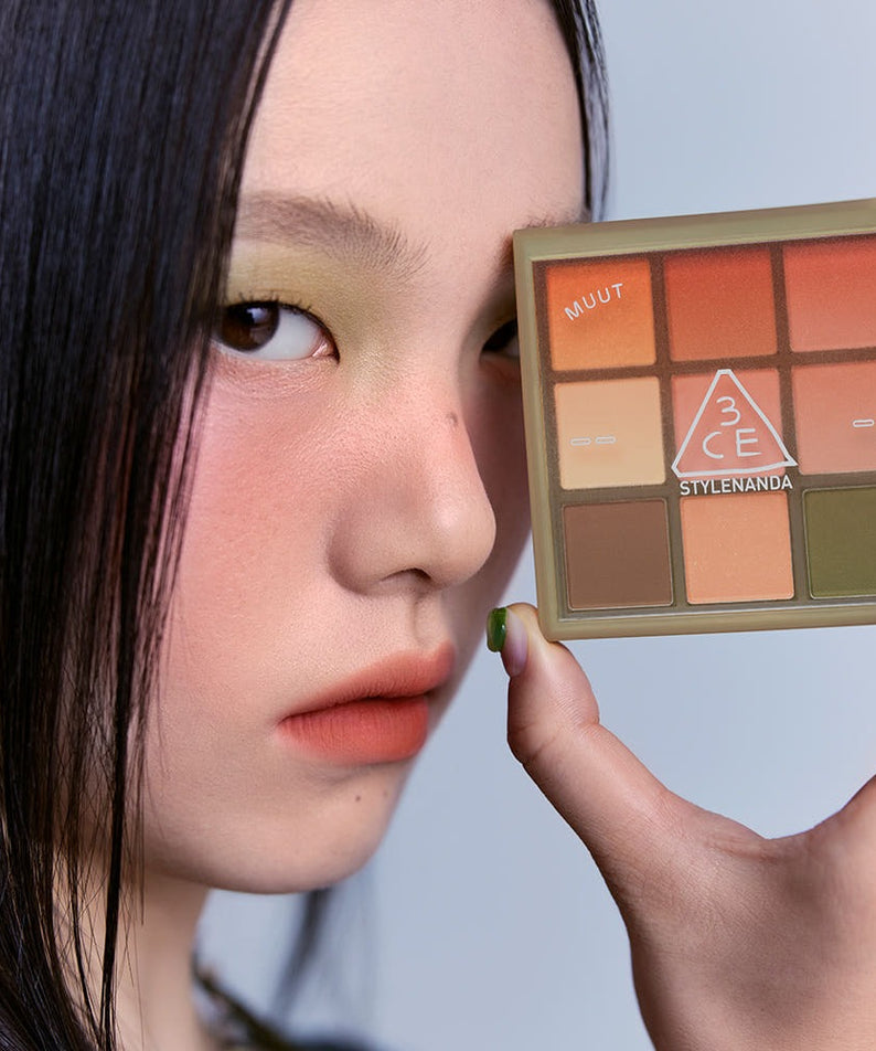 Palette de fards à paupières 3CE Multi Eye Color Palette 7g tenue par une personne, maquillage tendance et couleurs vives.