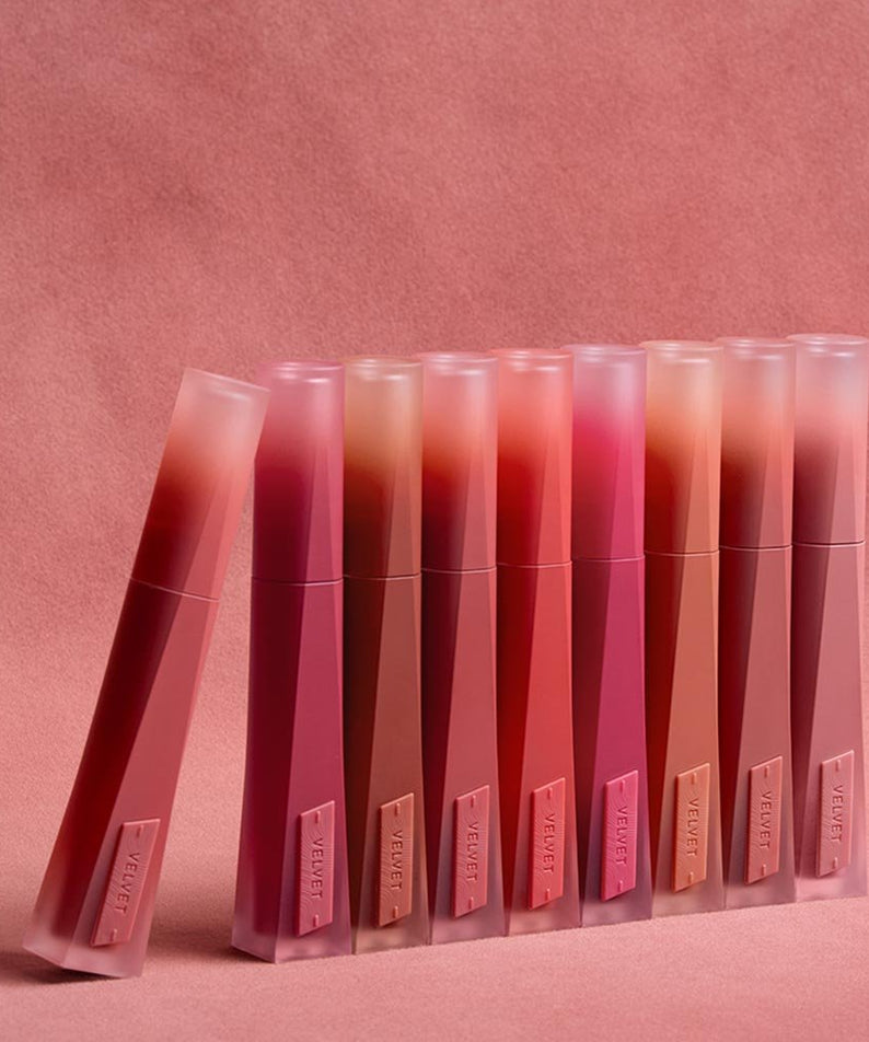 Gamme de teintes du 3CE Velvet Lip Tint Plush sur fond rose, maquillage élégant et moderne.