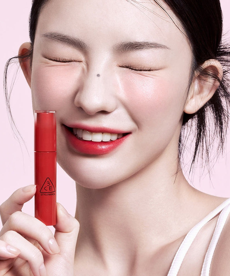 Modèle souriant tenant le 3CE Lazy Pop Lip Stain, mettant en valeur ses lèvres parfaitement colorées.