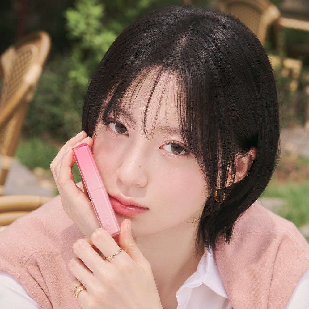 Portrait maquillage : ROMAND Sheer Tinted Stick de ROMAND, jeune femme en extérieur, main tenant le stick rose.