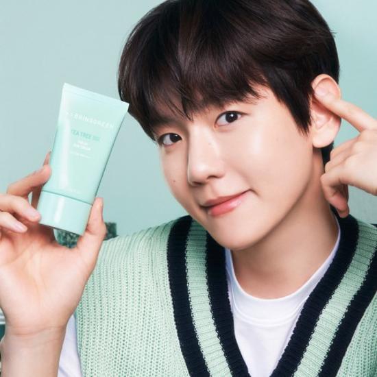 BRINGGREEN Teatree Cica Fresh Sun Cream 50ml, tube crème solaire sur fond bleu, jeune tenant le produit (contexte visuel).