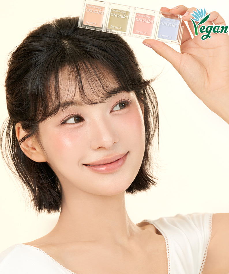 Femme souriante tenant DEAR.A Single Concealer 10 Colors, produit cosmétique vegan. Conçu pour un teint parfait et naturel.