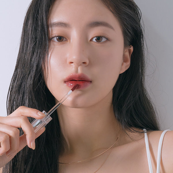 ROMAND Glasting Water Tint, femme appliquant un gloss rosé sur lèvres, tenue légère, fond clair, photo beauté ROMAND.