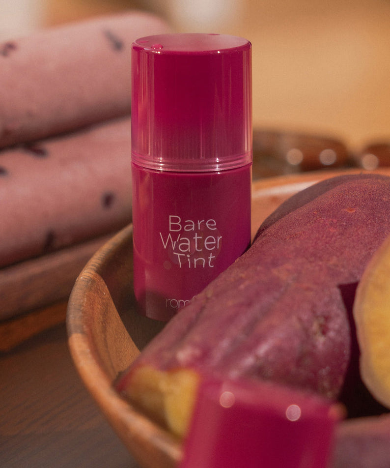 ROMAND Bare Water Tint de la marque ROMAND, flacon rose sur table avec accessoires cosmétiques, ambiance beauté