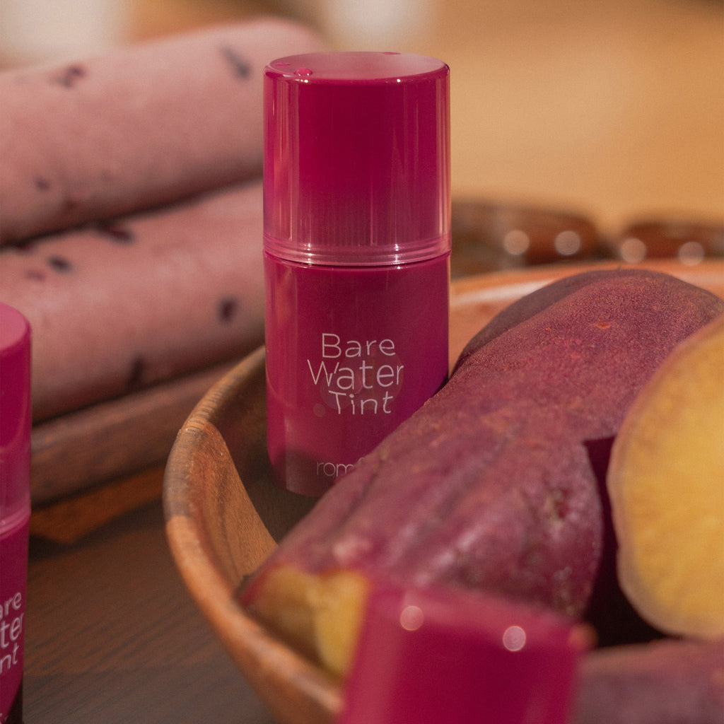 ROMAND Bare Water Tint de la marque ROMAND, flacon rose sur table avec accessoires cosmétiques, ambiance beauté