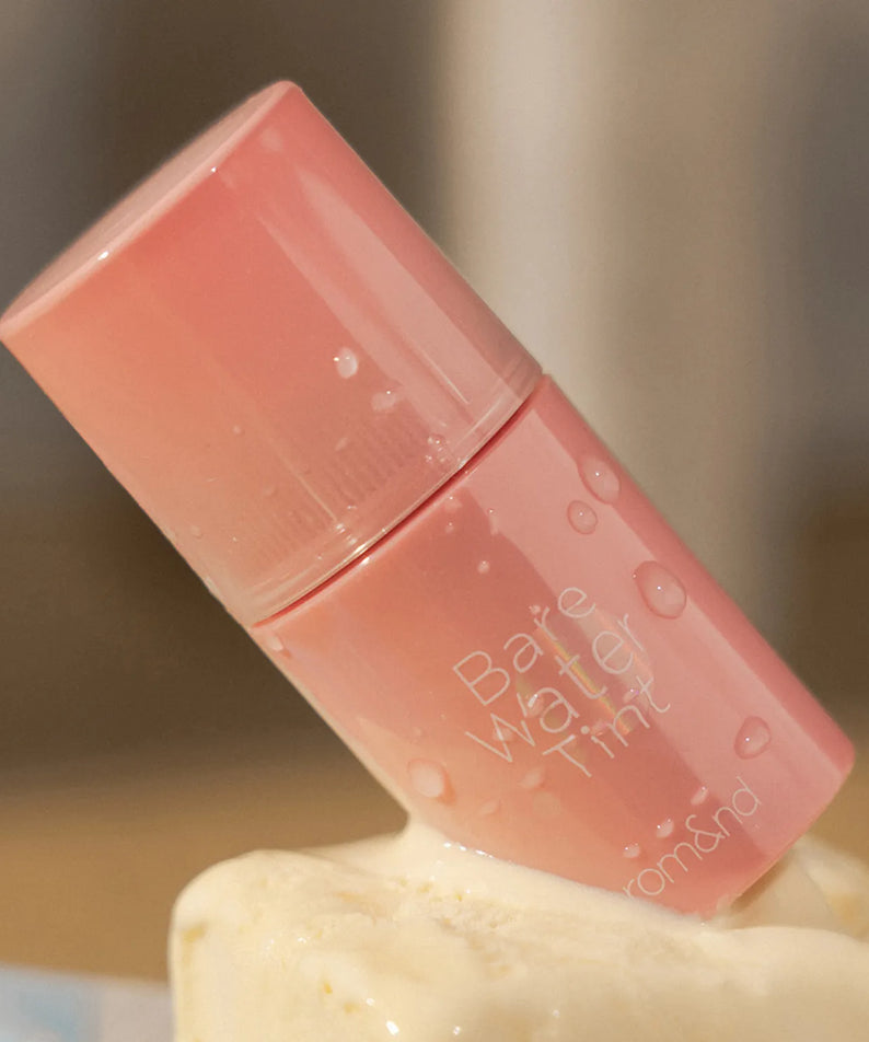 ROMAND Bare Water Tint, flacon de teint effet eau rose pâle sur fond crème, marque ROMAND, photo produit beauté.