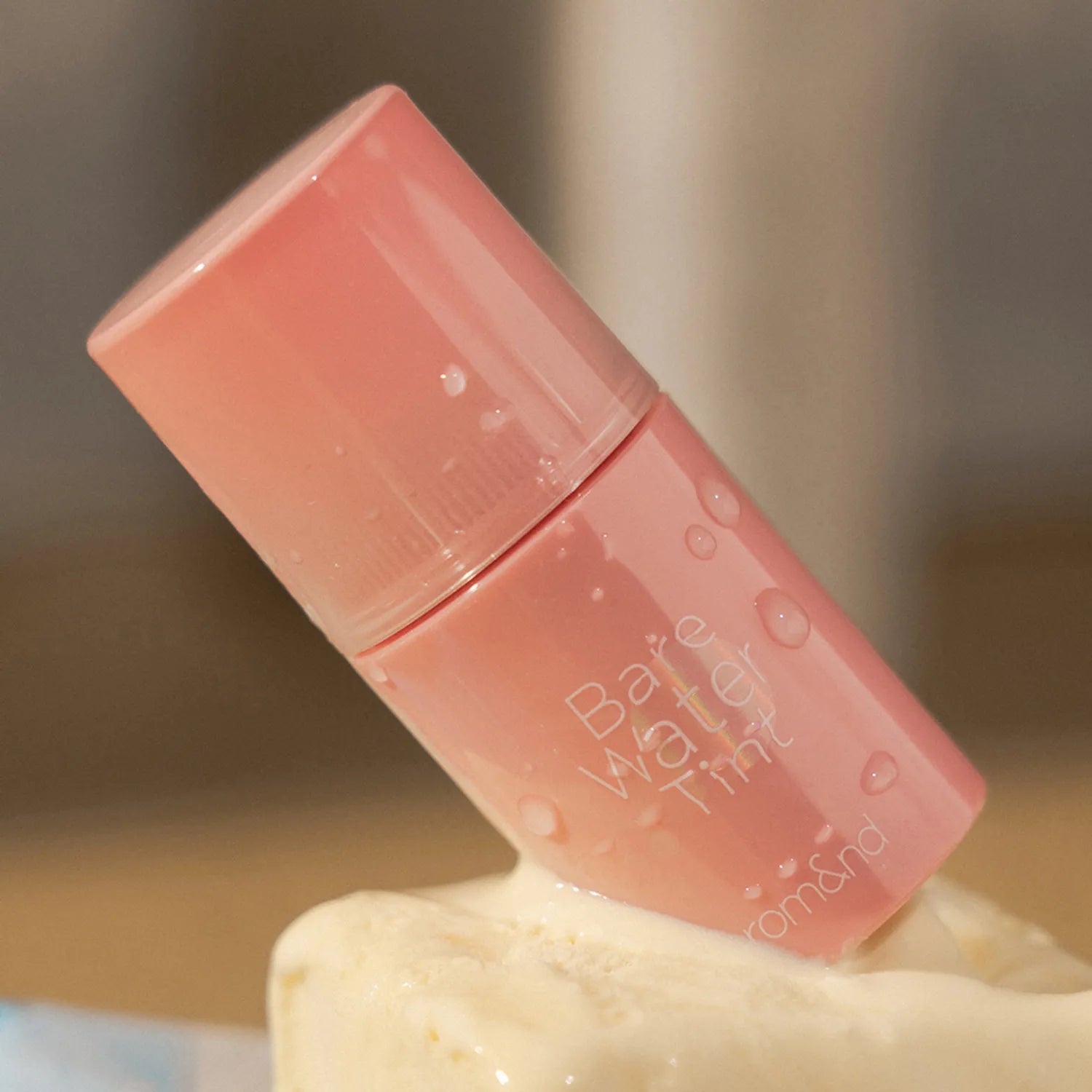 ROMAND Bare Water Tint, flacon de teint effet eau rose pâle sur fond crème, marque ROMAND, photo produit beauté.